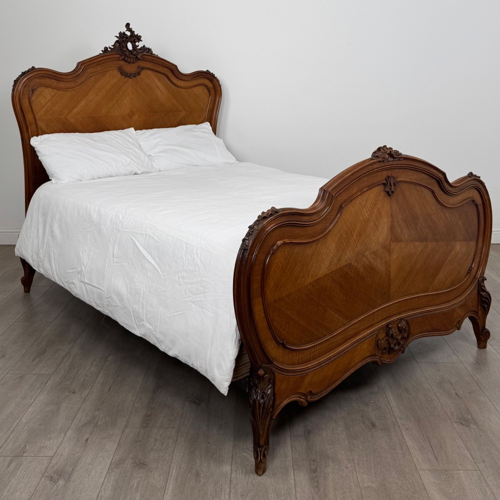 A 19th-century French walnut double bed featuring a carved crest headboard, matching footboard with parquetry panels, and short cabriole legs.