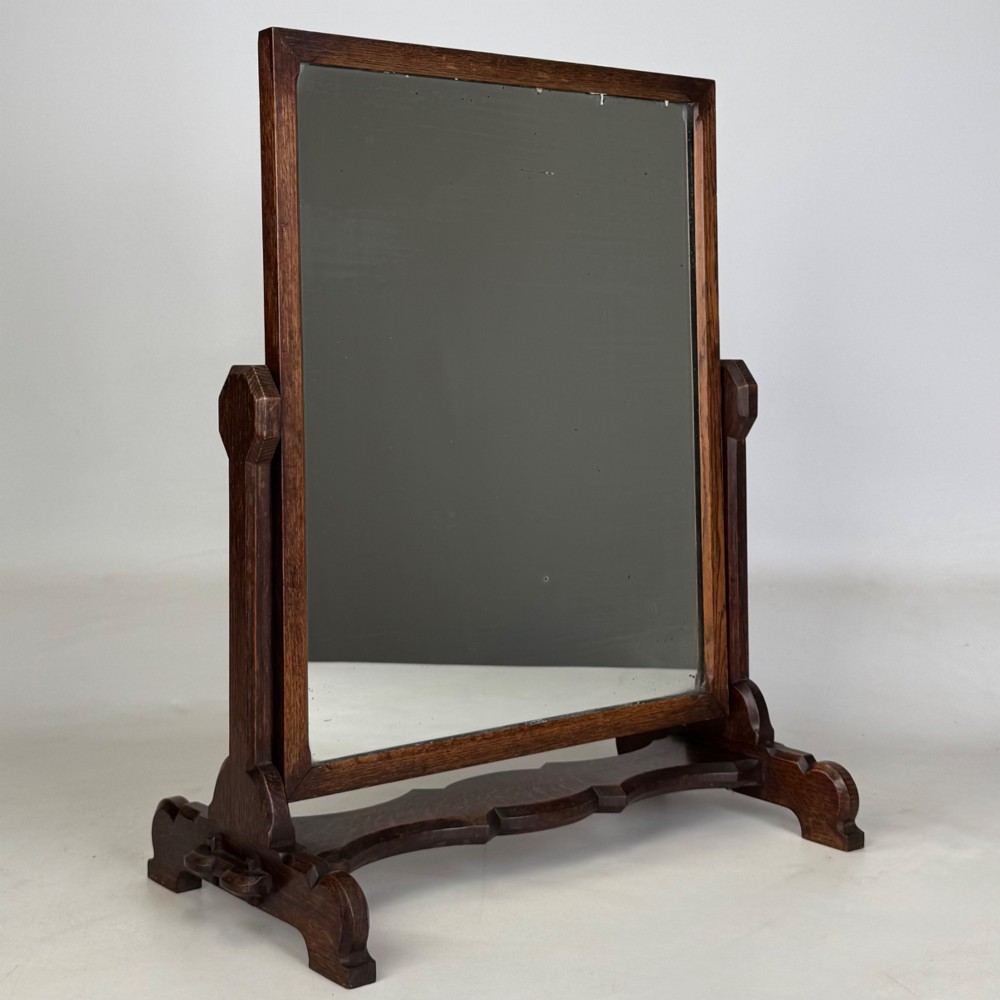 An early 20th-century Arts and Crafts dark oak dressing table mirror set on a shaped base with a swivel frame.