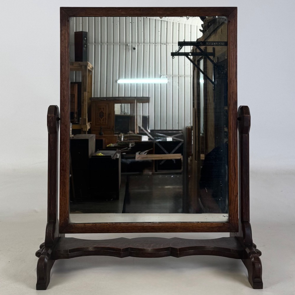 An early 20th-century Arts and Crafts dark oak dressing table mirror set on a shaped base with a swivel frame. View II