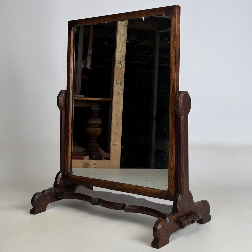 An early 20th-century Arts and Crafts dark oak dressing table mirror set on a shaped base with a swivel frame. View III