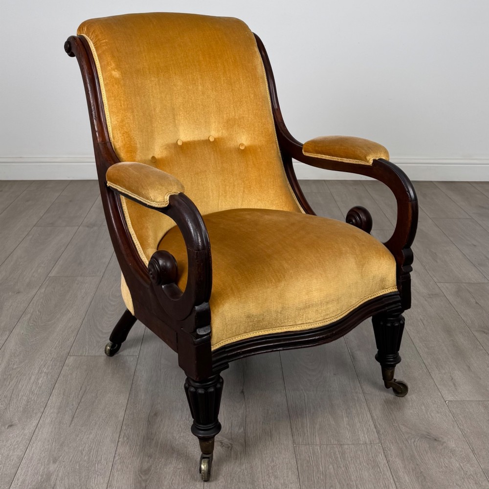 A pair of 19th-century William IV mahogany armchairs upholstered in mustard gold velvet featuring carved scroll arms and turned front legs on brass castors. View VIII