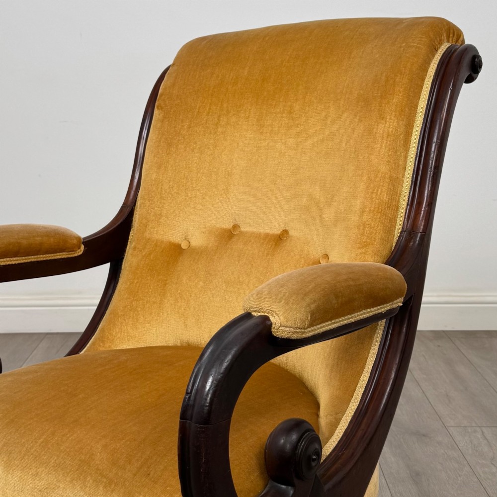 A pair of 19th-century William IV mahogany armchairs upholstered in mustard gold velvet featuring carved scroll arms and turned front legs on brass castors. View XI