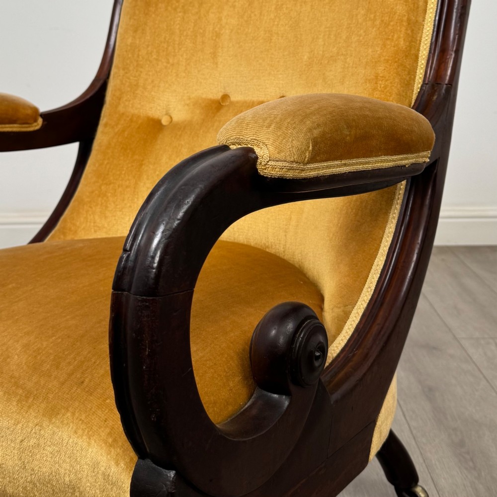 A pair of 19th-century William IV mahogany armchairs upholstered in mustard gold velvet featuring carved scroll arms and turned front legs on brass castors. View XII