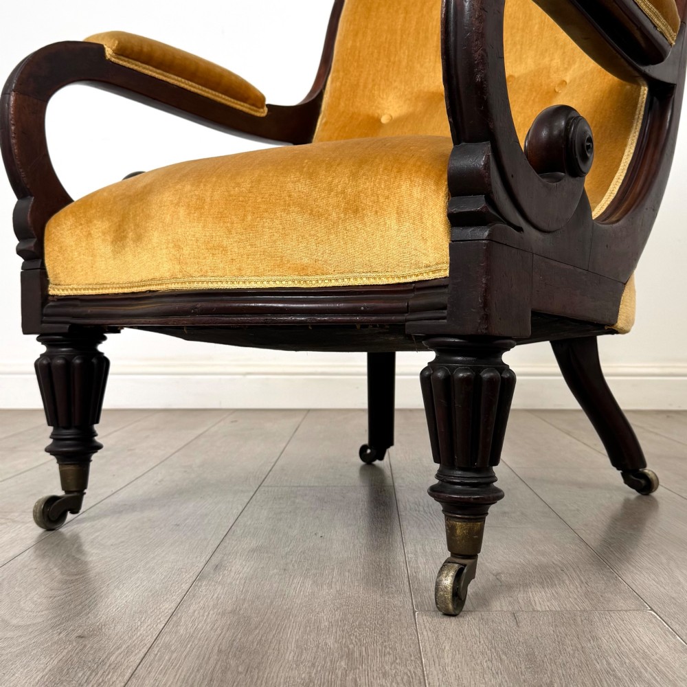 A pair of 19th-century William IV mahogany armchairs upholstered in mustard gold velvet featuring carved scroll arms and turned front legs on brass castors. View XIII