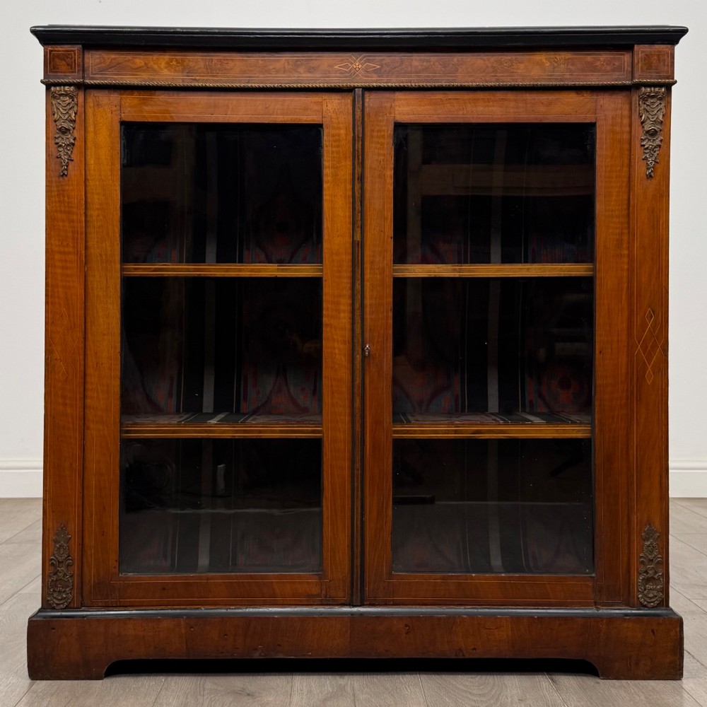 A 19th-century Victorian burr walnut pier cabinet featuring two glass panel doors, brass mounts, marquetry inlay, and a plinth base.