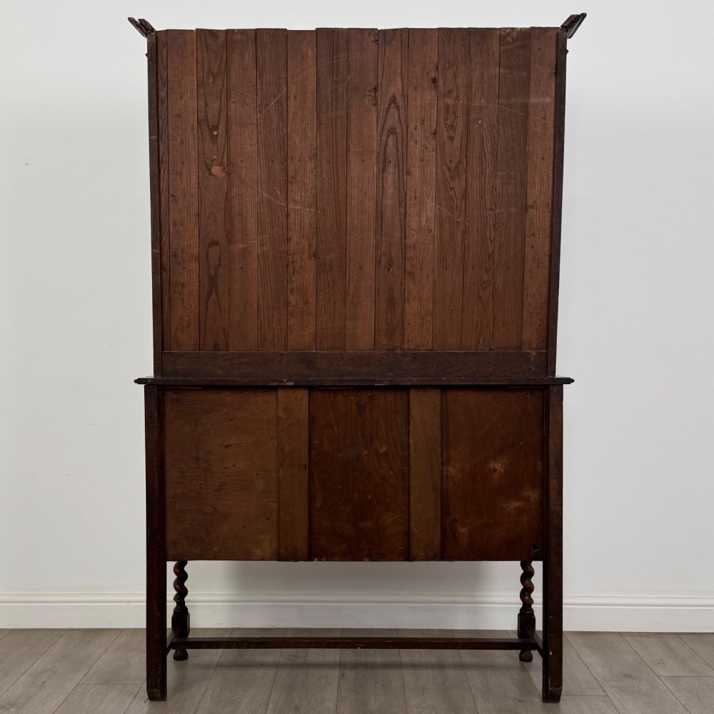 An early 20th-century dark oak Welsh dresser featuring a three-tier open plate rack mounted on a base cabinet with two drawers, geometric panel doors, and barley twist legs. View VI