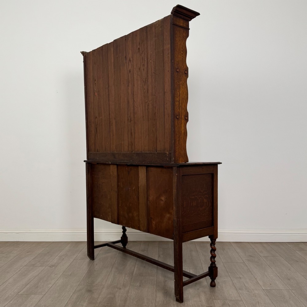 An early 20th-century dark oak Welsh dresser featuring a three-tier open plate rack mounted on a base cabinet with two drawers, geometric panel doors, and barley twist legs. View VII