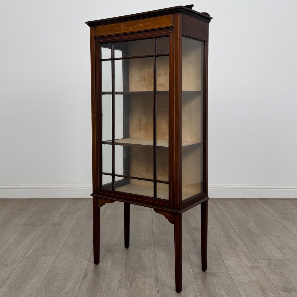 A slender Edwardian mahogany display cabinet featuring a single glazed door with geometric glazing bars, floral inlay on the top frieze, and long tapered legs. View III