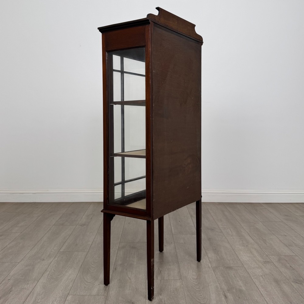A slender Edwardian mahogany display cabinet featuring a single glazed door with geometric glazing bars, floral inlay on the top frieze, and long tapered legs. View V