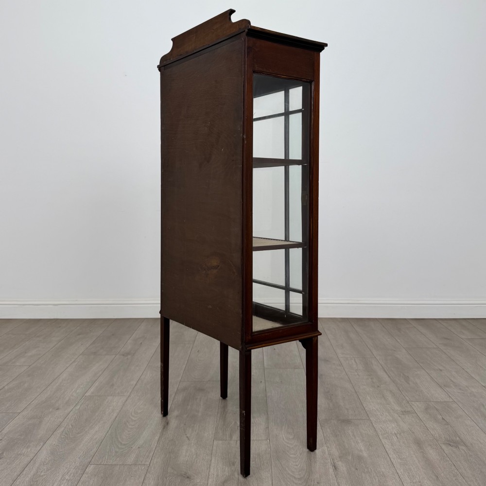 A slender Edwardian mahogany display cabinet featuring a single glazed door with geometric glazing bars, floral inlay on the top frieze, and long tapered legs. View VII