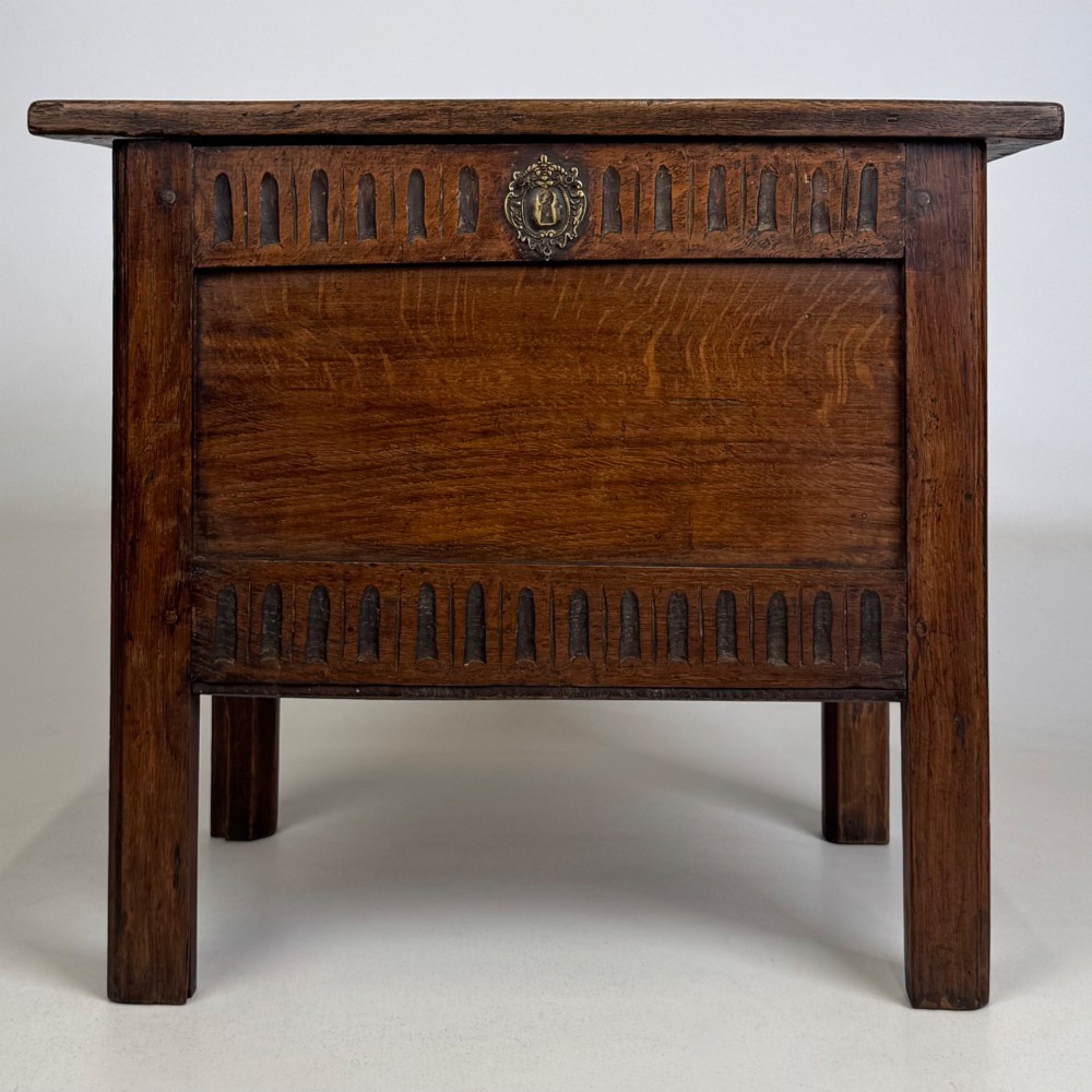 An 18th-century small oak coffer chest featuring carved vertical fluting along the top and bottom rails, a central decorative brass escutcheon, and straight squared legs.