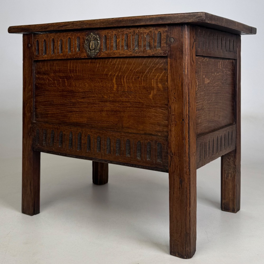 An 18th-century small oak coffer chest featuring carved vertical fluting along the top and bottom rails, a central decorative brass escutcheon, and straight squared legs. View II