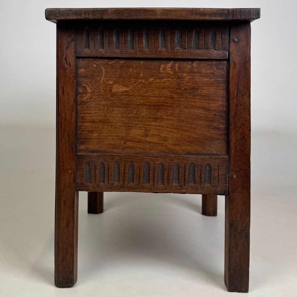 An 18th-century small oak coffer chest featuring carved vertical fluting along the top and bottom rails, a central decorative brass escutcheon, and straight squared legs. View III