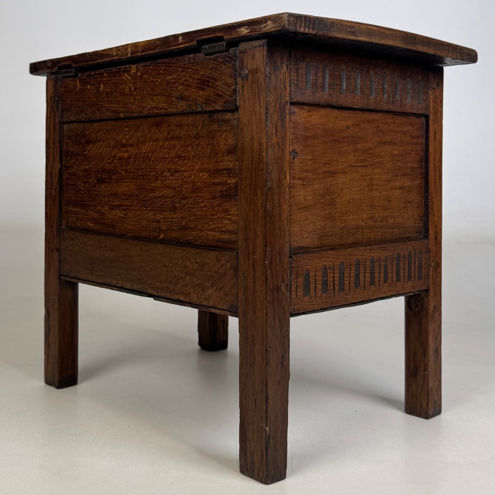 An 18th-century small oak coffer chest featuring carved vertical fluting along the top and bottom rails, a central decorative brass escutcheon, and straight squared legs. View VI