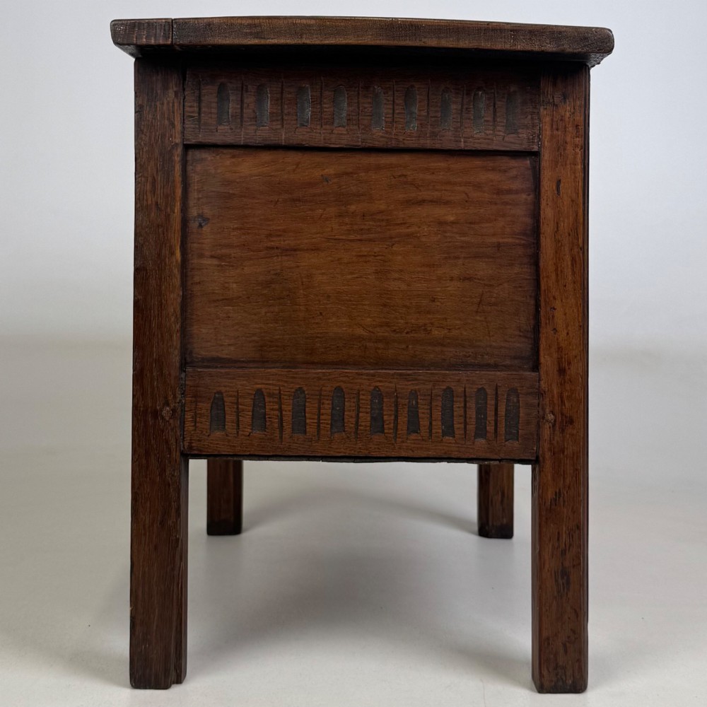 An 18th-century small oak coffer chest featuring carved vertical fluting along the top and bottom rails, a central decorative brass escutcheon, and straight squared legs. View VII