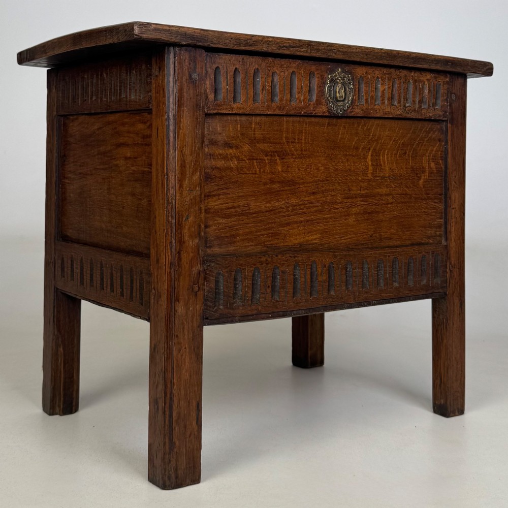 An 18th-century small oak coffer chest featuring carved vertical fluting along the top and bottom rails, a central decorative brass escutcheon, and straight squared legs. View VIII