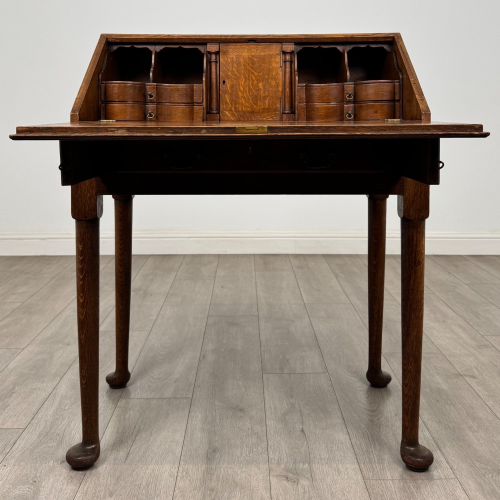 A golden oak slant-front writing bureau standing on four slender legs with pad feet, featuring a single lower drawer with drop handles and a hinged writing slope. View II