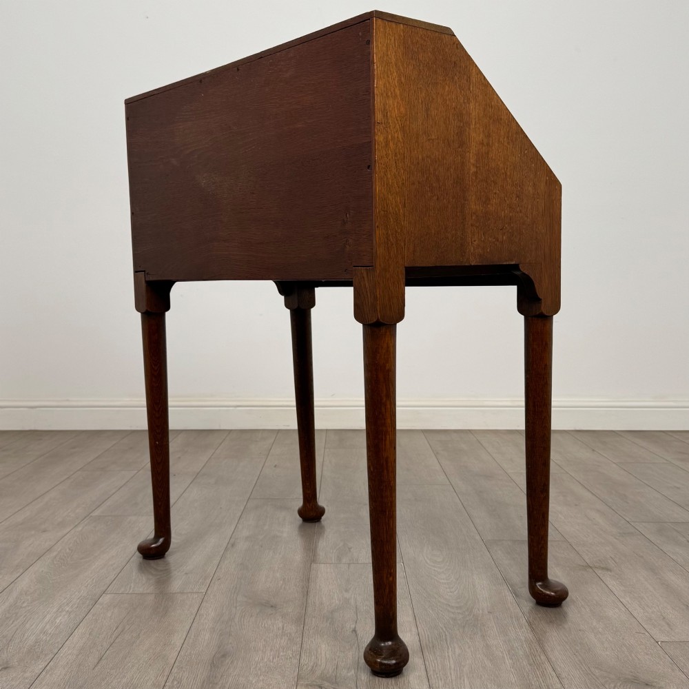 A golden oak slant-front writing bureau standing on four slender legs with pad feet, featuring a single lower drawer with drop handles and a hinged writing slope. View VII
