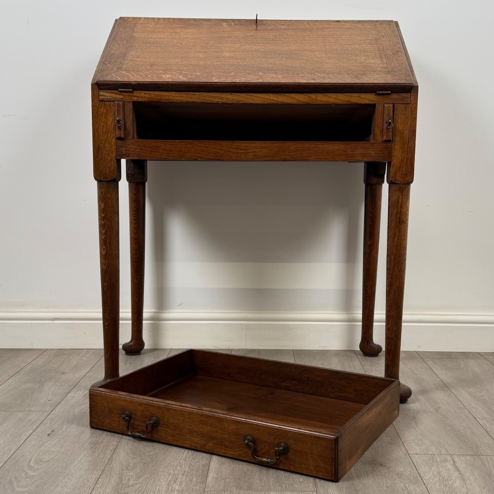 A golden oak slant-front writing bureau standing on four slender legs with pad feet, featuring a single lower drawer with drop handles and a hinged writing slope. View XII