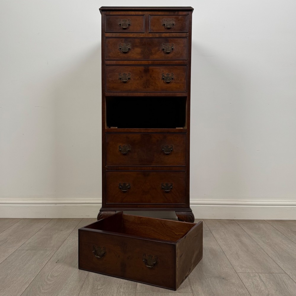 A tall, narrow dark brown burr walnut chest of drawers featuring brass handles and carved cabriole legs. View X