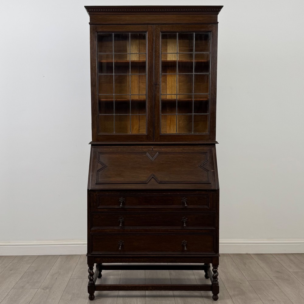 A tall 20th-century Jacobean Revival dark oak bureau bookcase with a leaded glass cabinet above a slant-front writing desk and three lower drawers. View II
