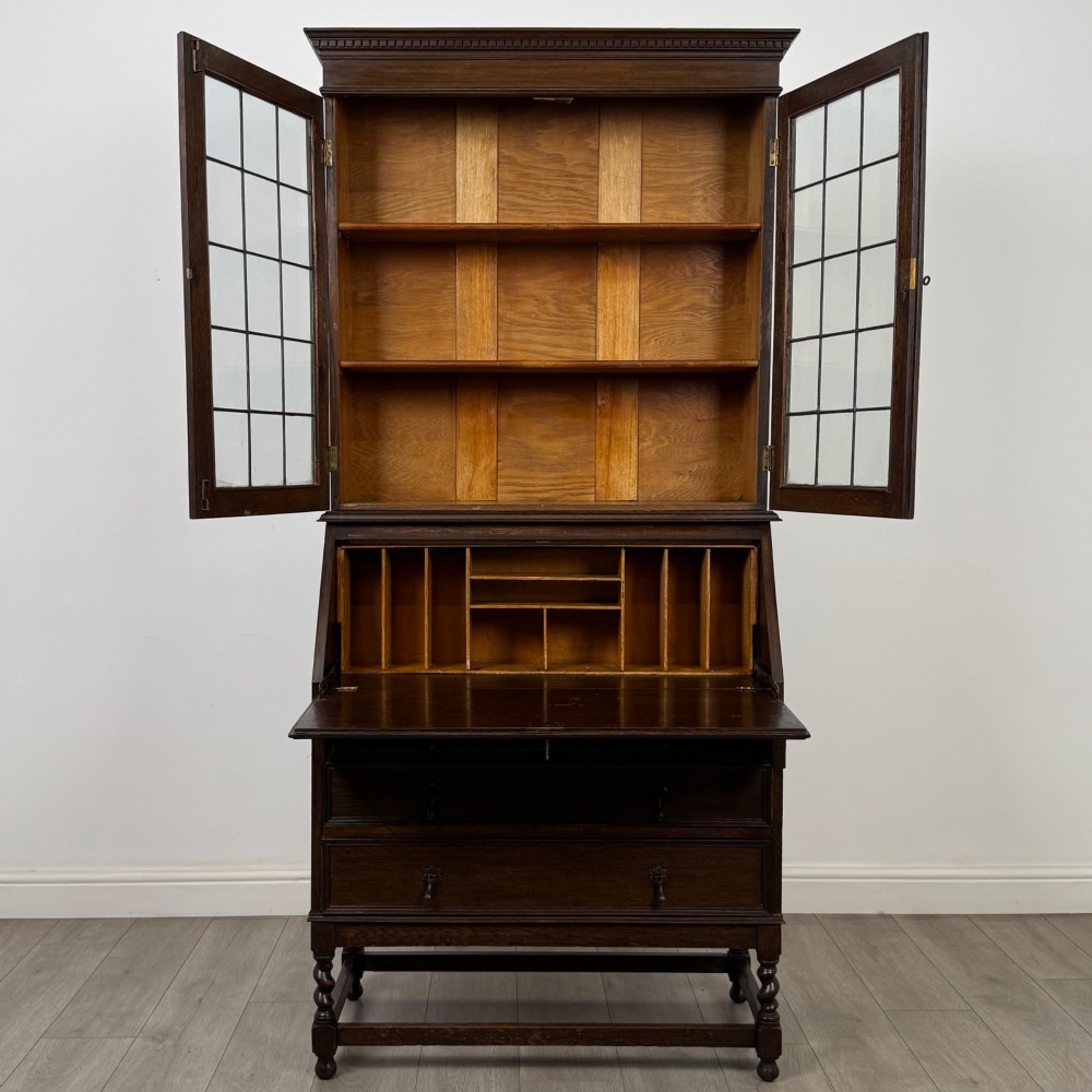 A tall 20th-century Jacobean Revival dark oak bureau bookcase with a leaded glass cabinet above a slant-front writing desk and three lower drawers. View III