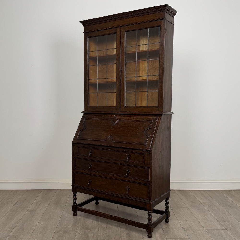 A tall 20th-century Jacobean Revival dark oak bureau bookcase with a leaded glass cabinet above a slant-front writing desk and three lower drawers. View IV