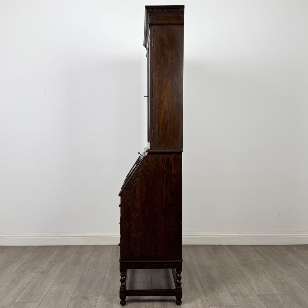 A tall 20th-century Jacobean Revival dark oak bureau bookcase with a leaded glass cabinet above a slant-front writing desk and three lower drawers. View V