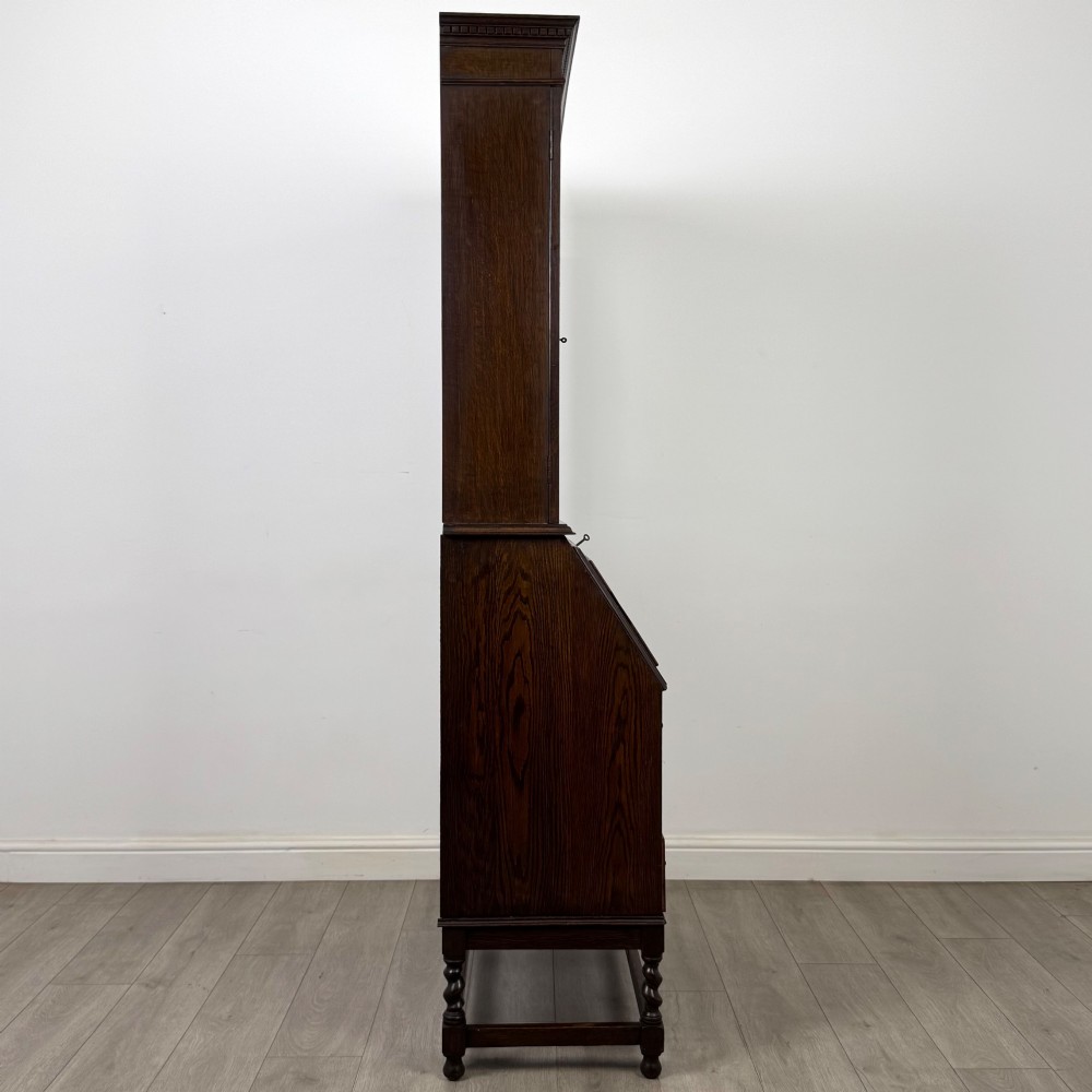 A tall 20th-century Jacobean Revival dark oak bureau bookcase with a leaded glass cabinet above a slant-front writing desk and three lower drawers. View IX