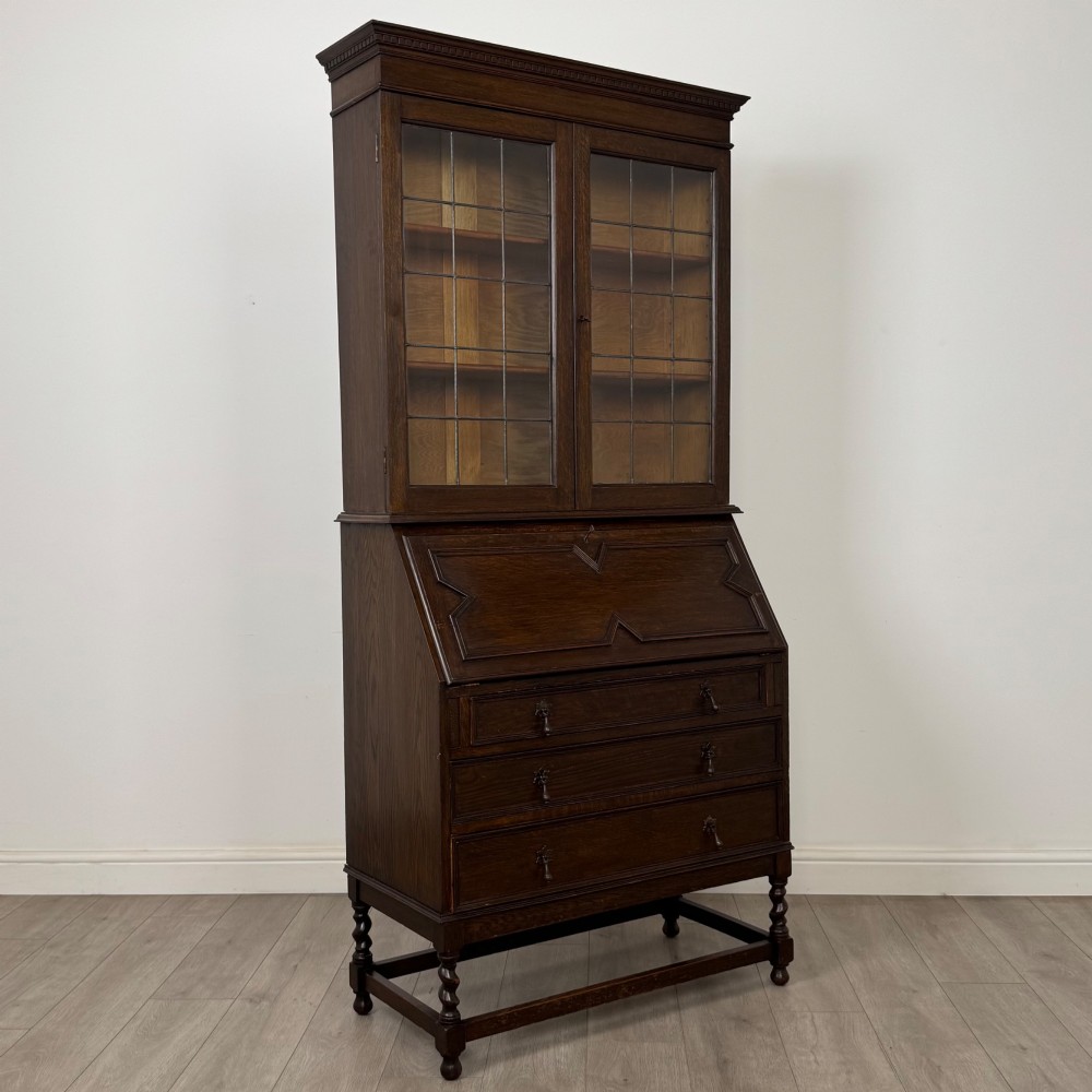 A tall 20th-century Jacobean Revival dark oak bureau bookcase with a leaded glass cabinet above a slant-front writing desk and three lower drawers. View X