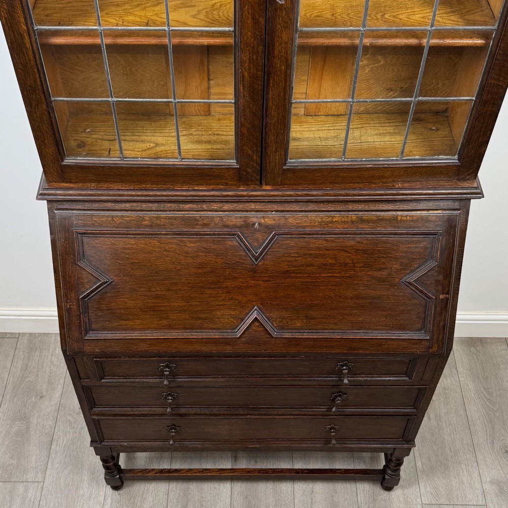 A tall 20th-century Jacobean Revival dark oak bureau bookcase with a leaded glass cabinet above a slant-front writing desk and three lower drawers. View XI