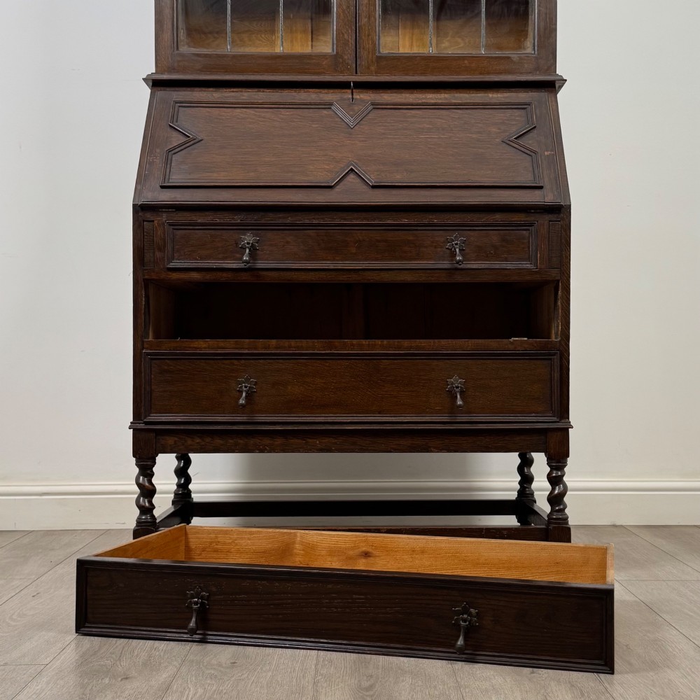 A tall 20th-century Jacobean Revival dark oak bureau bookcase with a leaded glass cabinet above a slant-front writing desk and three lower drawers. View XIII