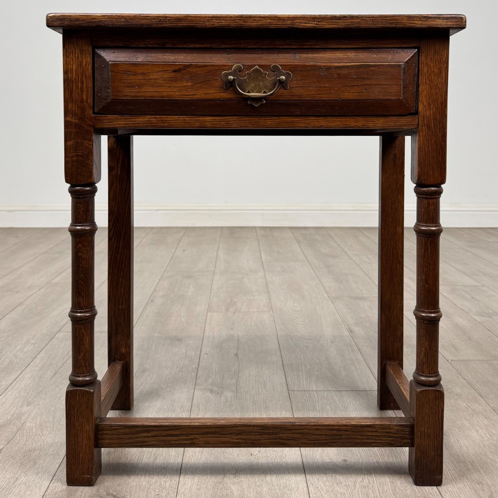 A small dark oak side table featuring a single drawer with a brass handle, turned front legs, and lower stretchers.