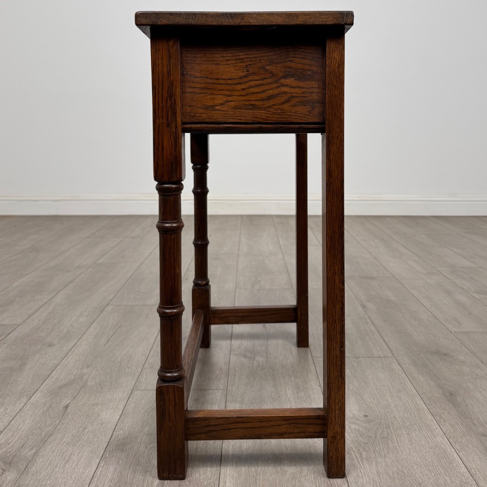 A small dark oak side table featuring a single drawer with a brass handle, turned front legs, and lower stretchers. View III