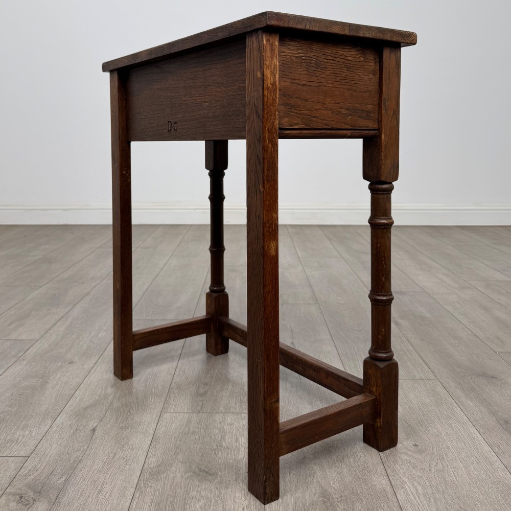 A small dark oak side table featuring a single drawer with a brass handle, turned front legs, and lower stretchers. View VI
