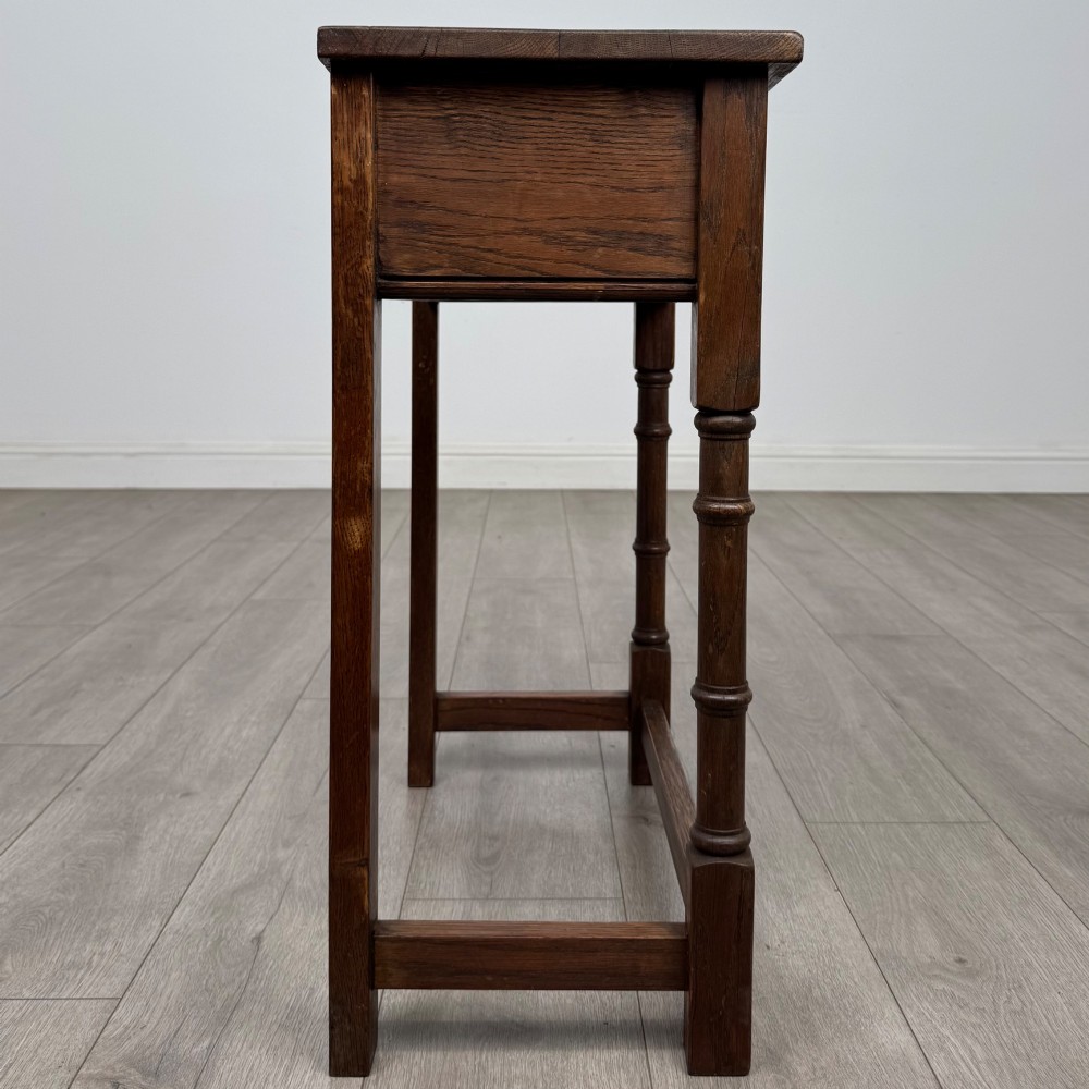A small dark oak side table featuring a single drawer with a brass handle, turned front legs, and lower stretchers. View VII