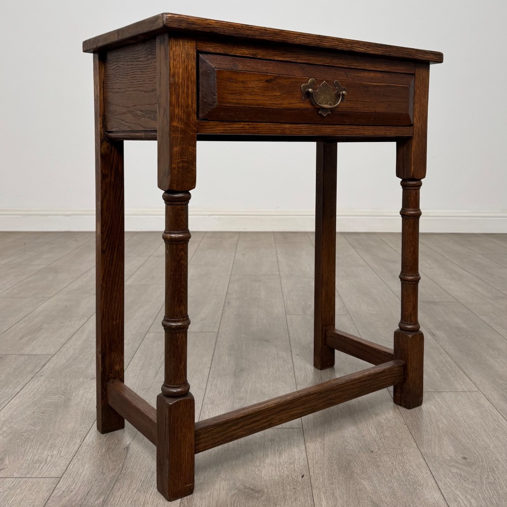 A small dark oak side table featuring a single drawer with a brass handle, turned front legs, and lower stretchers. View VIII