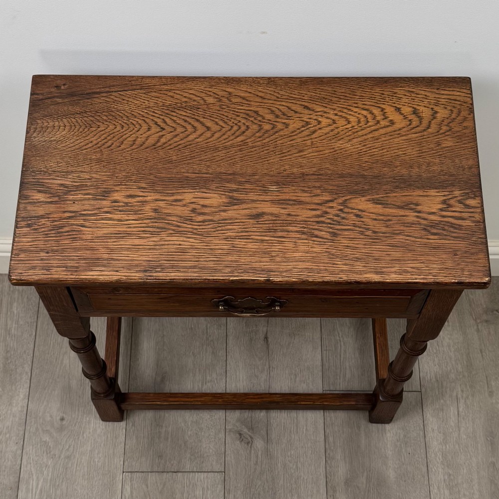 A small dark oak side table featuring a single drawer with a brass handle, turned front legs, and lower stretchers. View IX