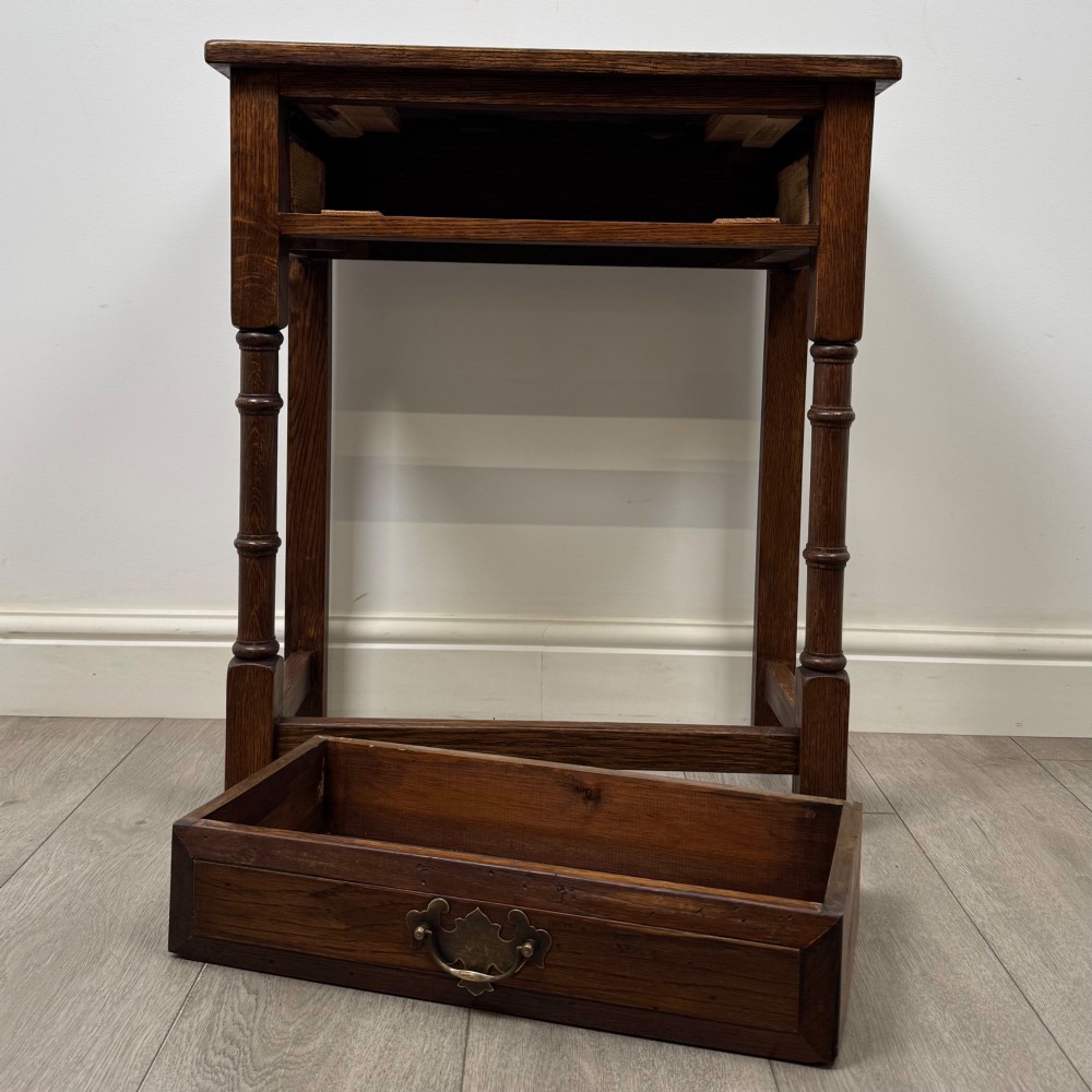A small dark oak side table featuring a single drawer with a brass handle, turned front legs, and lower stretchers. View X
