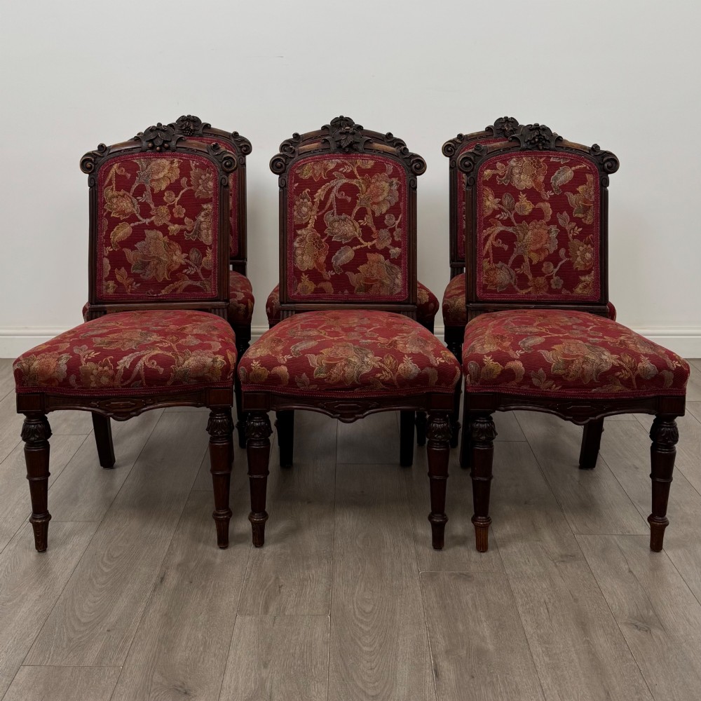 A set of six antique 19th-century Victorian oak dining chairs featuring carved crest rails and red patterned fabric upholstery.