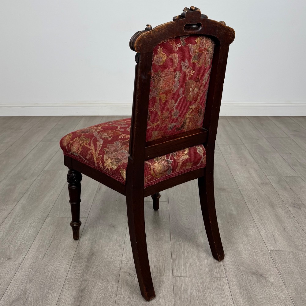 A set of six antique 19th-century Victorian oak dining chairs featuring carved crest rails and red patterned fabric upholstery. View III