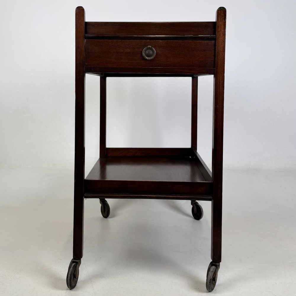 A two-tier dark mahogany Georgian style tea trolley featuring a single drawer with a brass ring handle and four castor wheels.