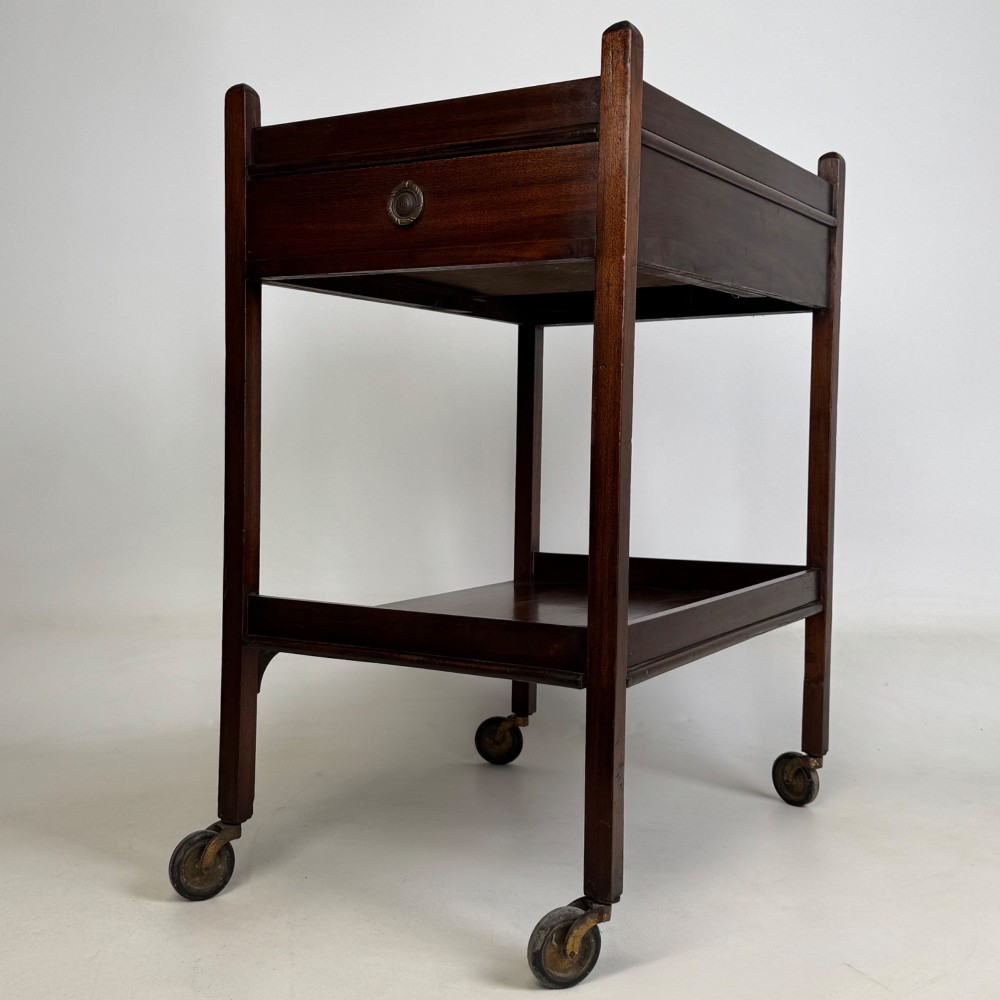 A two-tier dark mahogany Georgian style tea trolley featuring a single drawer with a brass ring handle and four castor wheels. View II