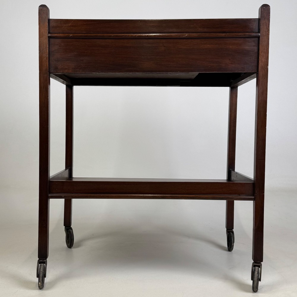 A two-tier dark mahogany Georgian style tea trolley featuring a single drawer with a brass ring handle and four castor wheels. View III