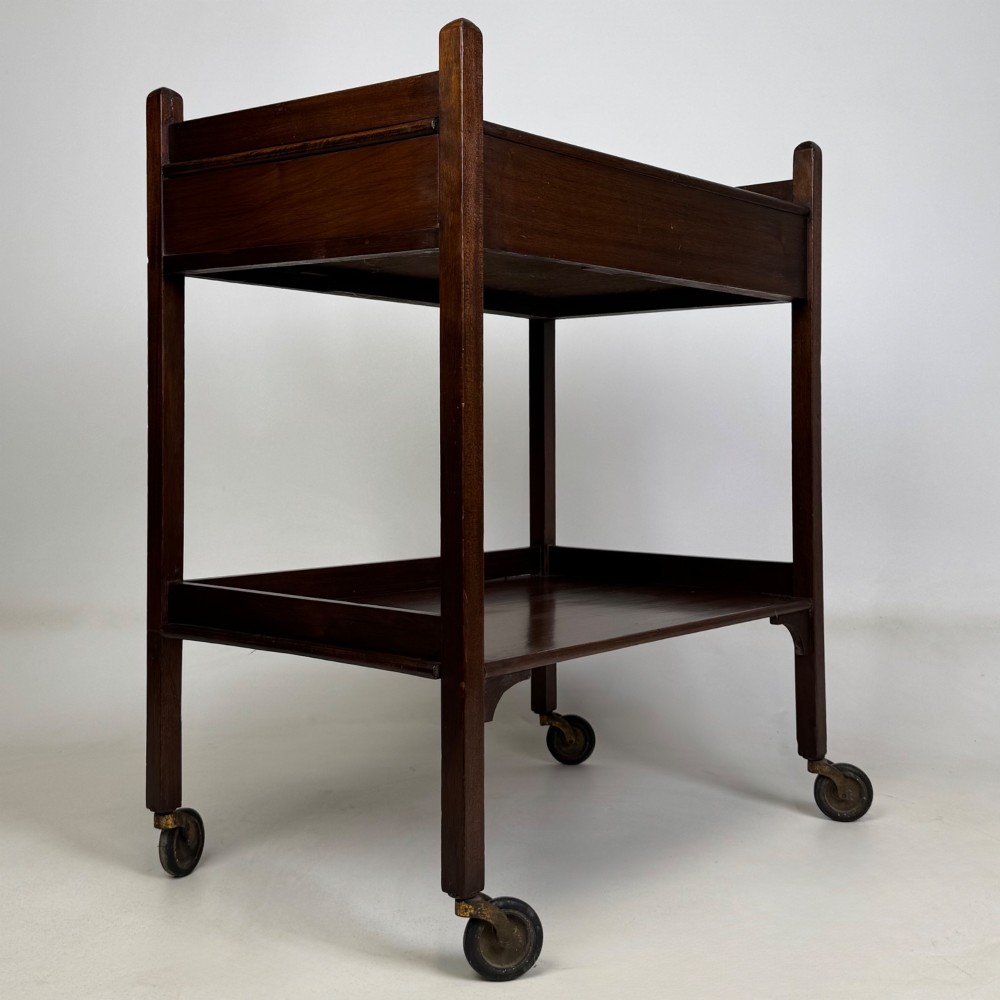 A two-tier dark mahogany Georgian style tea trolley featuring a single drawer with a brass ring handle and four castor wheels. View VI