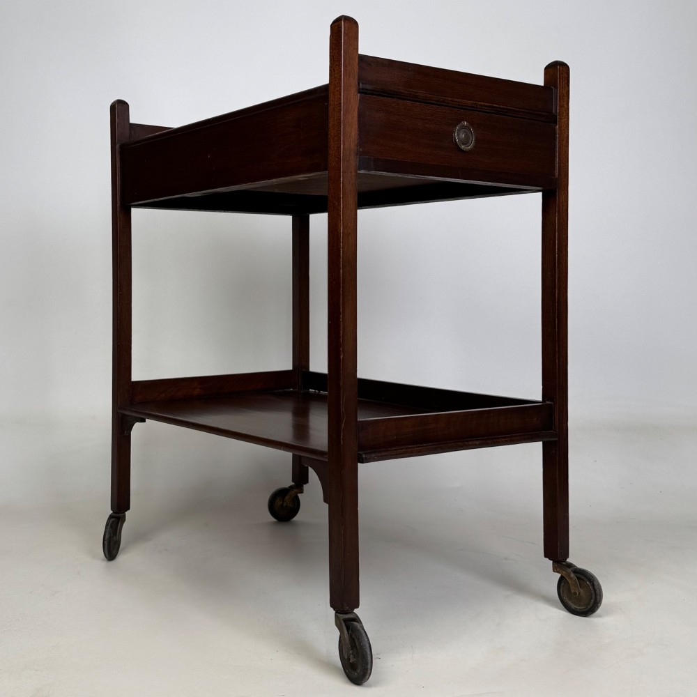A two-tier dark mahogany Georgian style tea trolley featuring a single drawer with a brass ring handle and four castor wheels. View VIII