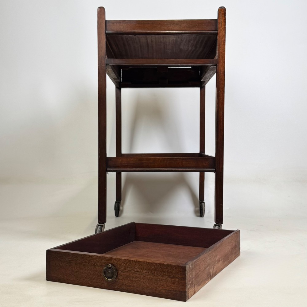 A two-tier dark mahogany Georgian style tea trolley featuring a single drawer with a brass ring handle and four castor wheels. View IX