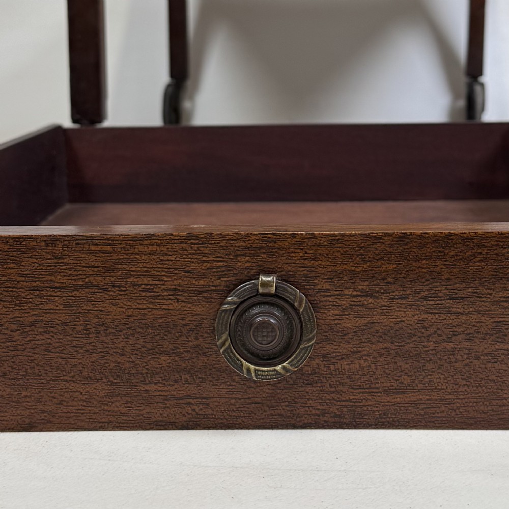 A two-tier dark mahogany Georgian style tea trolley featuring a single drawer with a brass ring handle and four castor wheels. View X