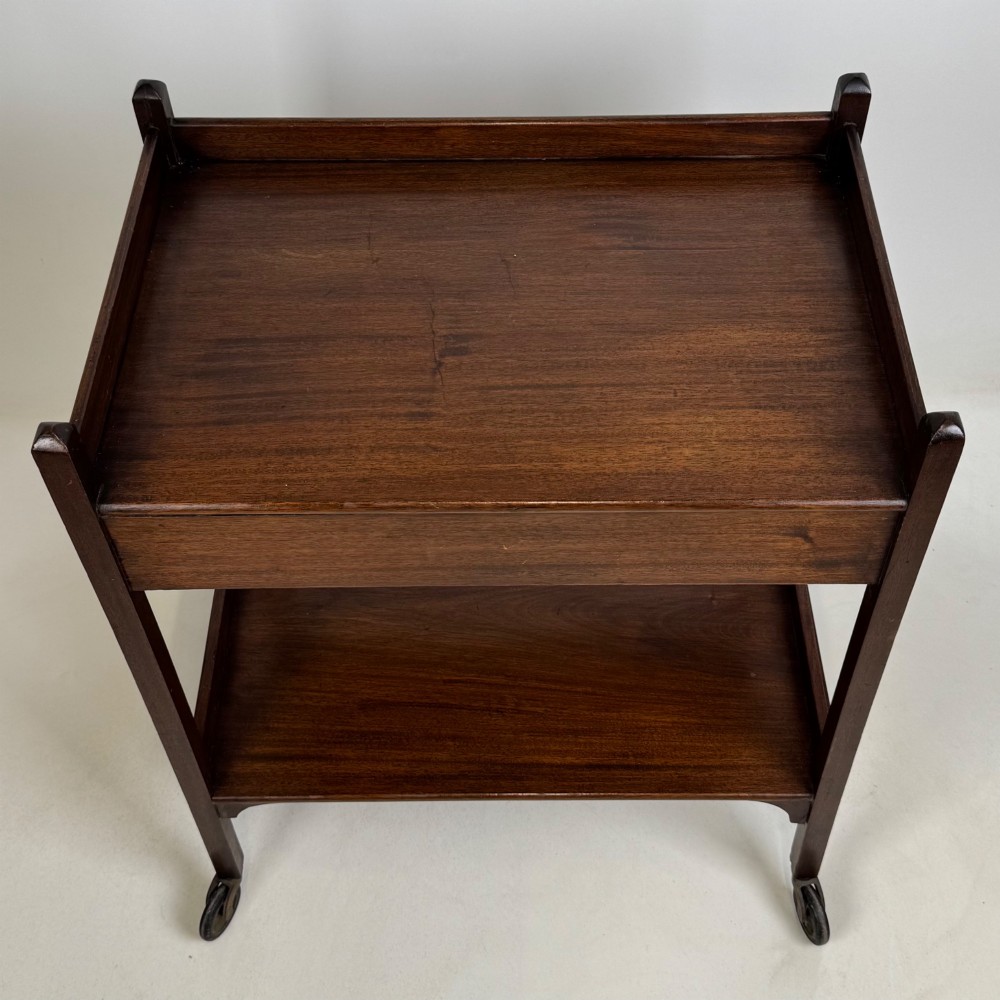 A two-tier dark mahogany Georgian style tea trolley featuring a single drawer with a brass ring handle and four castor wheels. View XI