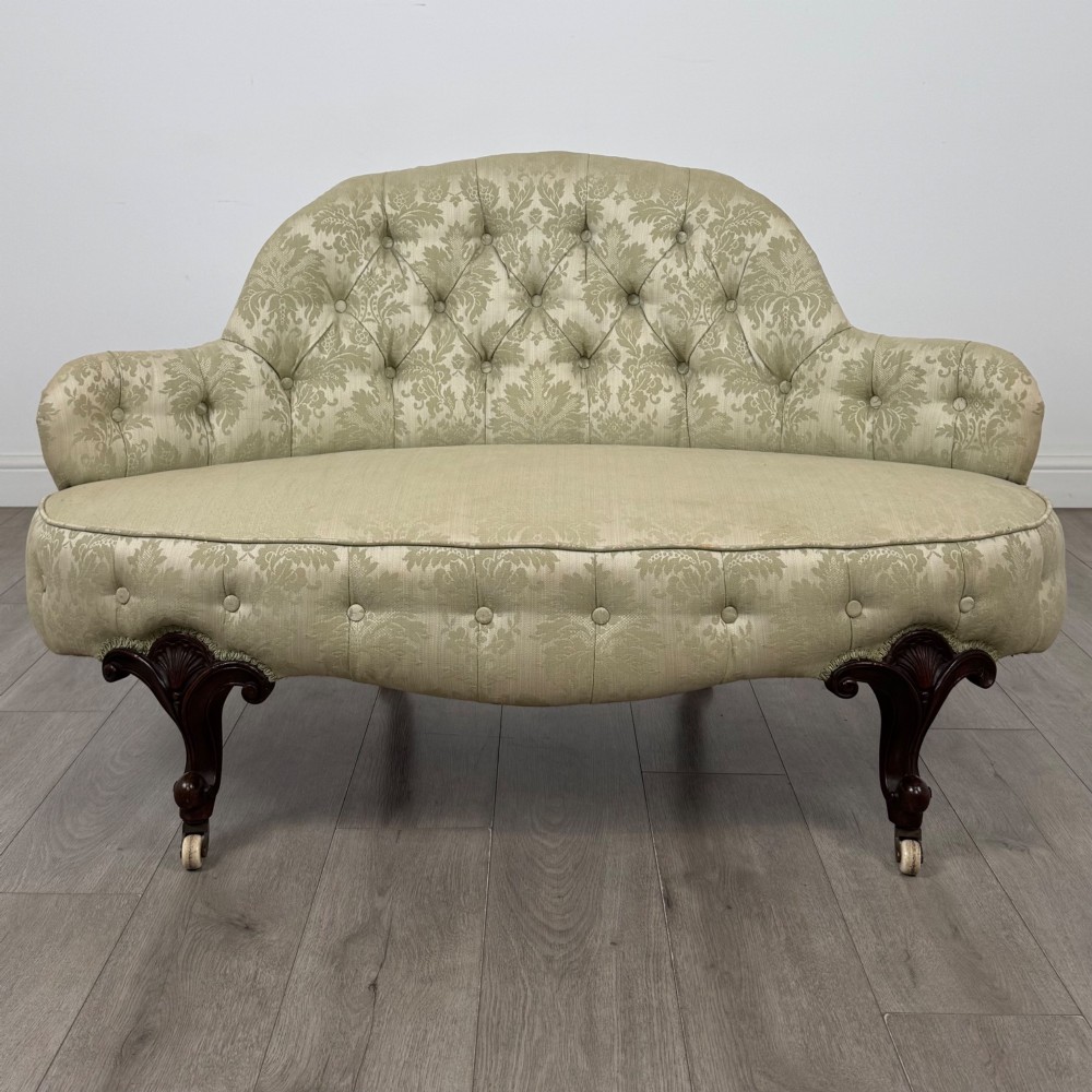 A 19th-century Victorian settee upholstered in sage green patterned damask with button-tufting and carved dark mahogany legs on ceramic castors.
